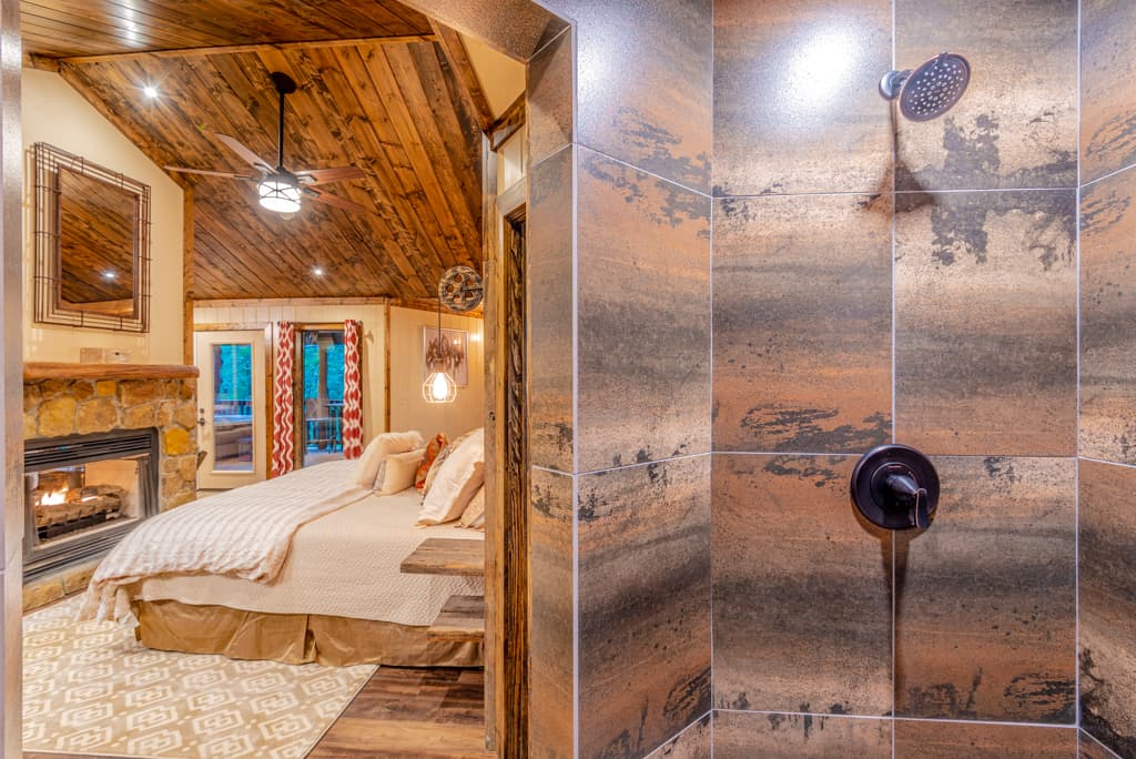 tile walk in shower with 2 heads next to king bed