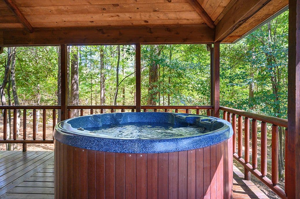 Covered patio with hot tub and wooden deck with forest views
