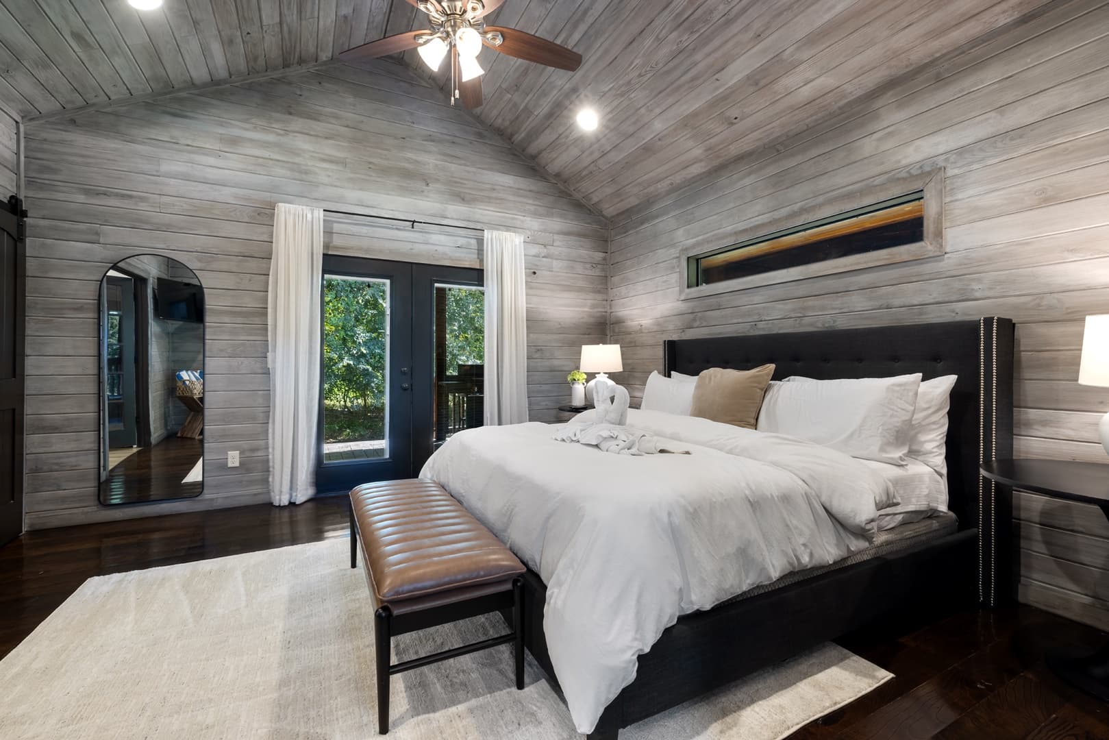 King bedroom with bench, side tables, lamps, and full length large mirror