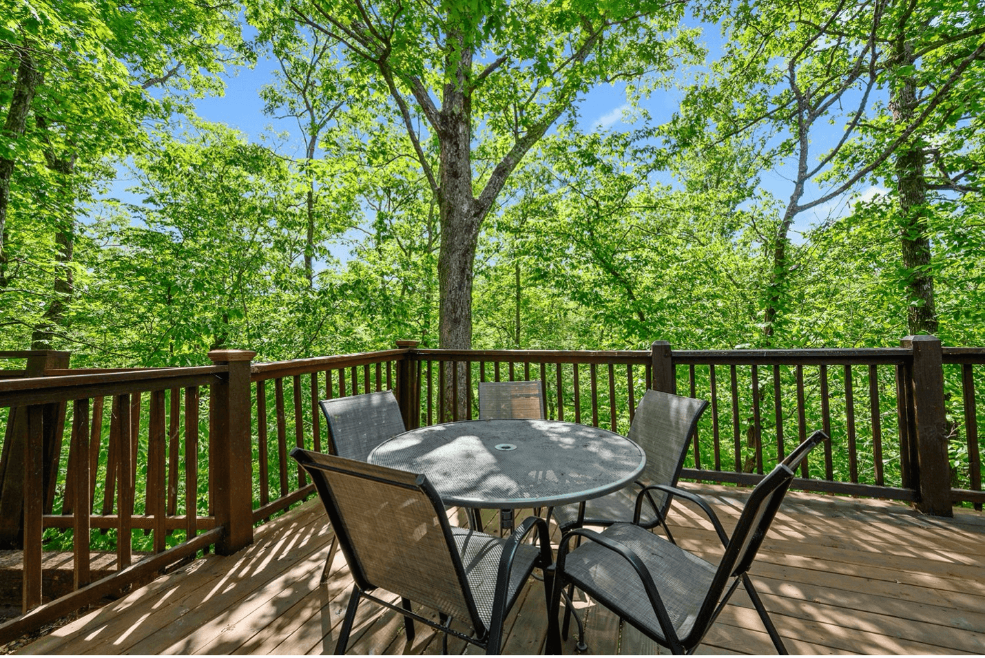 Log cabin with a green roof surrounded by trees under a clear blue sky.