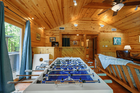 Cozy wooden cabin interior with foosball table, sofa, and warm lighting.