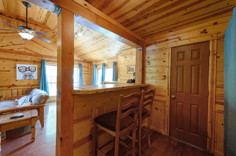 Cozy wooden cabin interior with a breakfast bar, stools, and natural light.