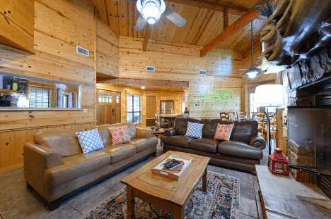 Cozy wooden cabin interior with leather sofas, a fireplace, and rustic decor.
