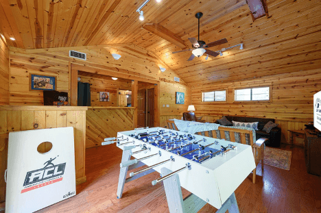 Cozy wooden cabin interior with a foosball table, sofa, and cornhole board game.