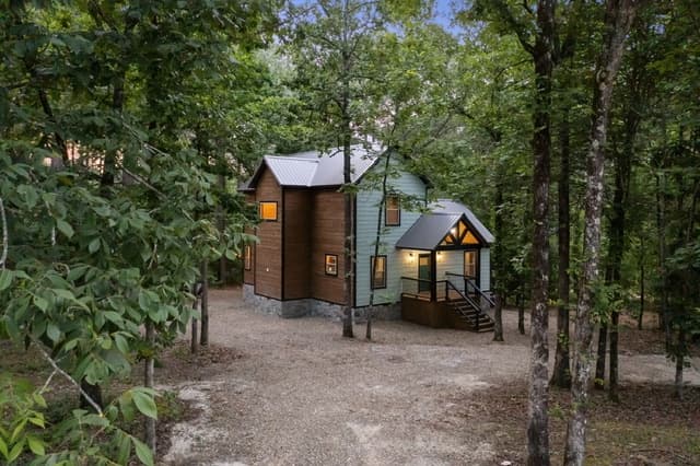A cozy two-story cabin with lit windows nestled among trees at dusk.