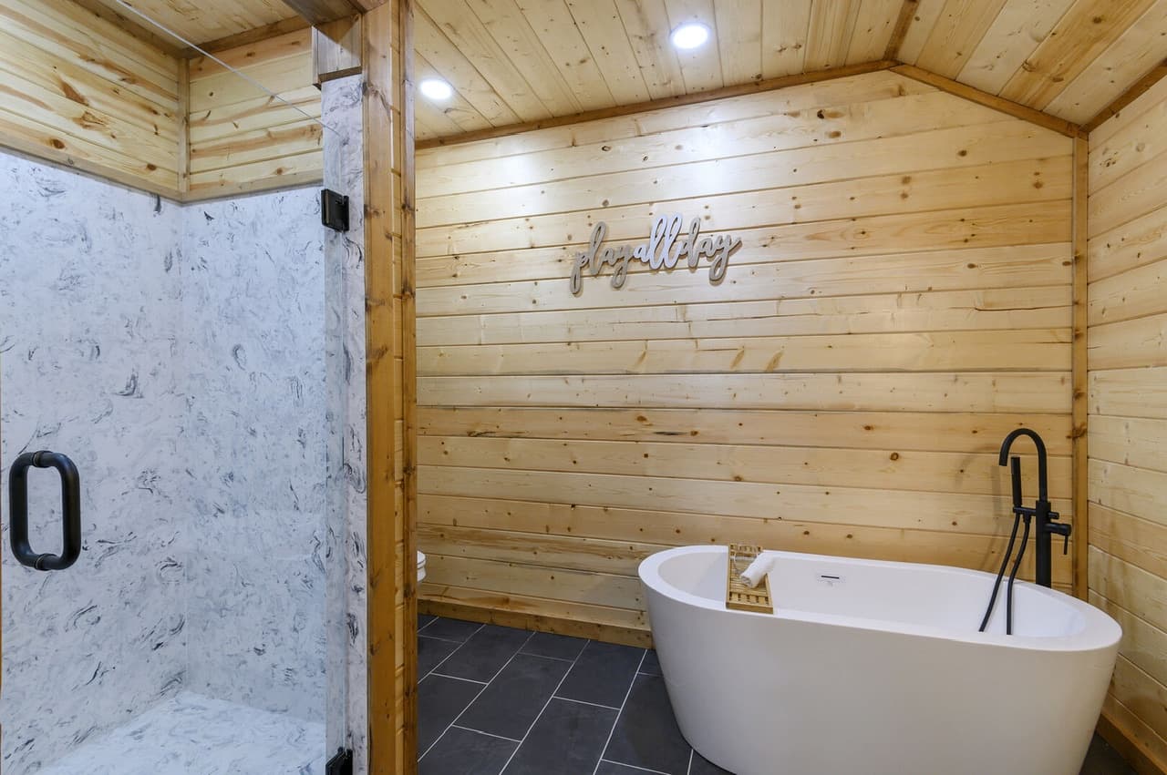 Modern bathroom with a freestanding tub, wooden walls, and textured grey shower area.