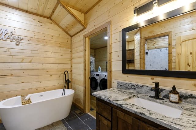 Modern bathroom with a standalone tub, wood walls, and a marble counter beside a laundry room.