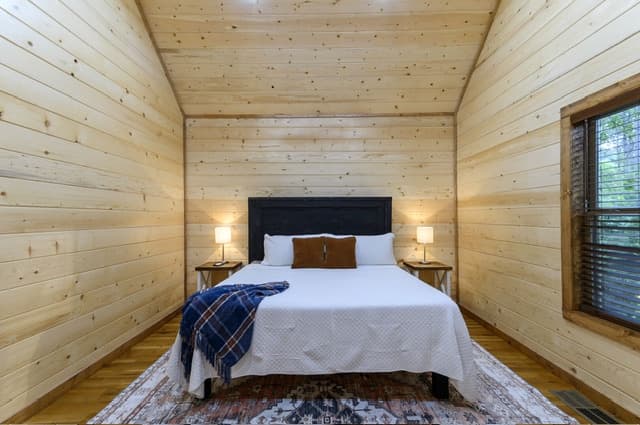Cozy wooden bedroom with a double bed, bedside lamps, and an area rug.
