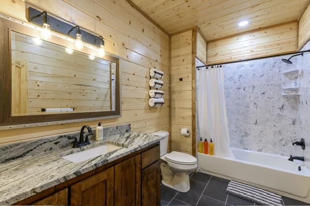 Rustic bathroom with wood paneling, granite countertop, and shower with curtain.
