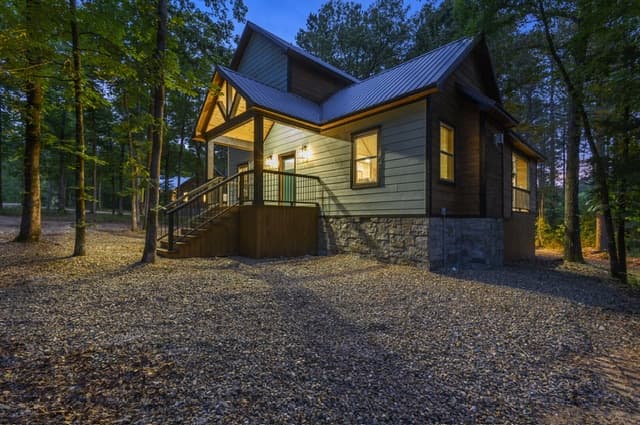 Twilight view of a cozy cabin with lit porch in a wooded area.