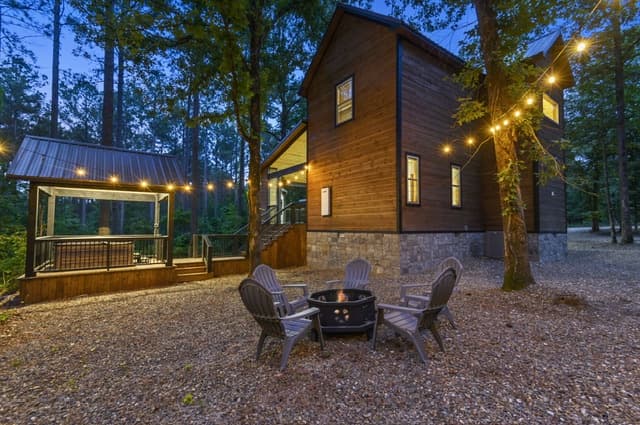 A cozy cabin with string lights at dusk, featuring an outdoor fire pit and seating area.