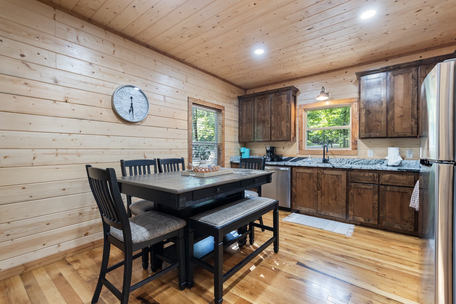 Cozy wooden cabin interior with sectional sofa, rug, and an open concept living room leading to kitchen.