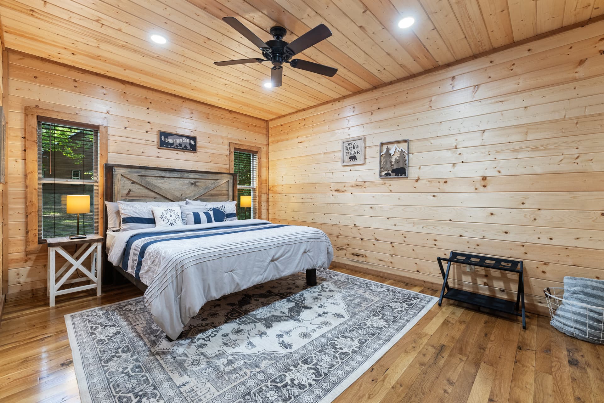 A cozy room featuring a lit fireplace with stone surround, flanked by wood walls and a window.