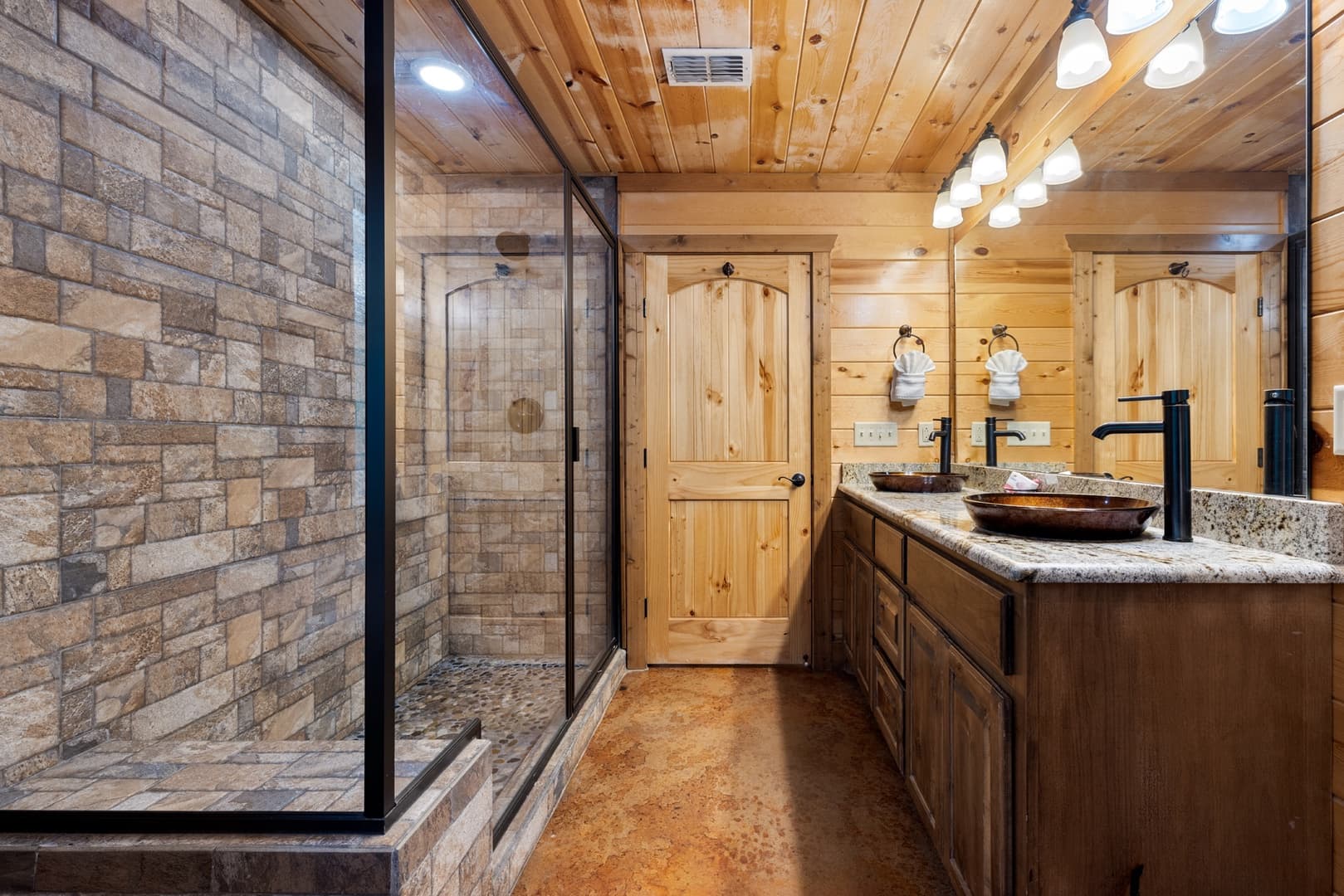 Rustic bathroom interior with stone tiles, wood paneling, and glass shower.