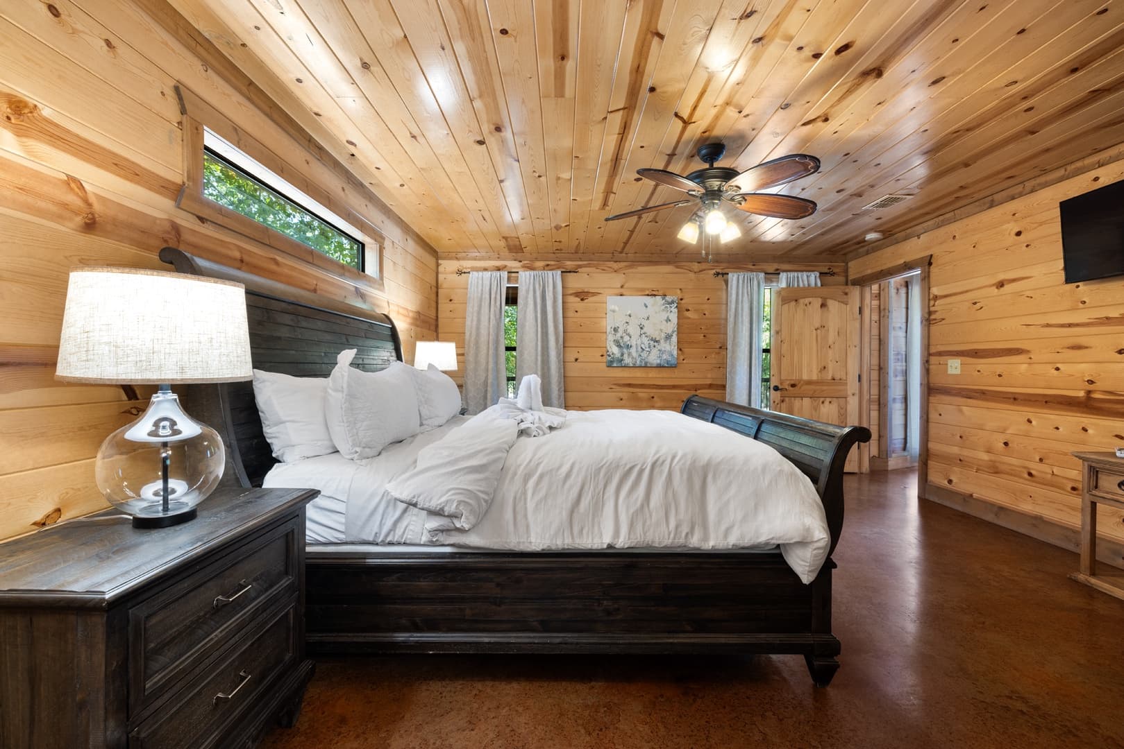 Cozy wooden cabin bedroom with a large bed, ceiling fan, and rustic furniture.