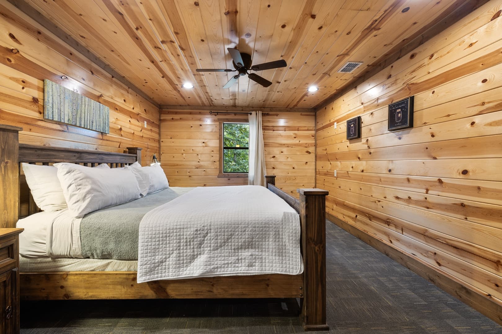 Cozy bedroom interior with wood-paneled walls, a large bed, and a ceiling fan.
