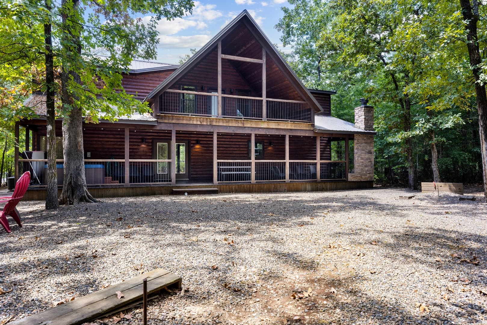 Wooden cabin with a spacious porch surrounded by trees and a gravel front yard.