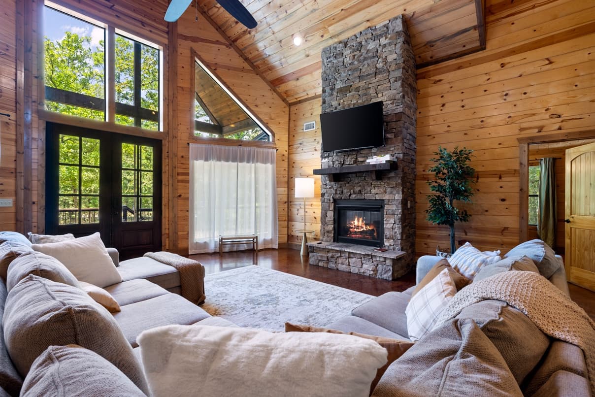 Cozy cabin living room with fireplace, large windows, and wooden interiors.