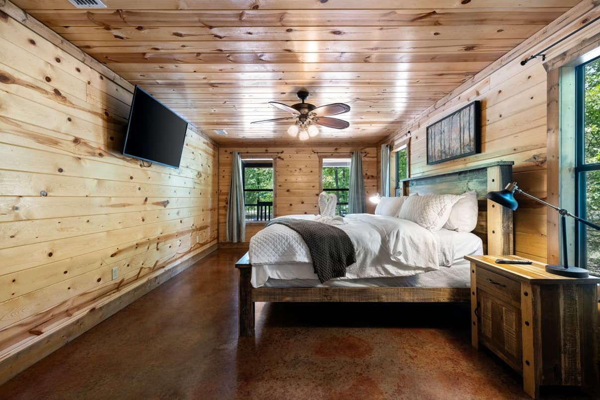 Cozy wooden cabin bedroom with a large bed, ceiling fan, and mounted TV.