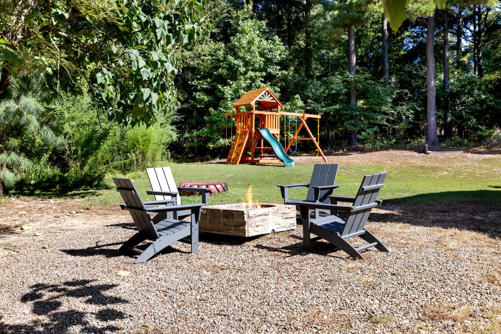 Firepit with chairs in gravel and the cabins kids playground off in the distance