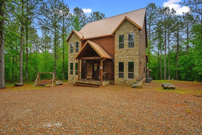 Front of log cabin and a swing next to it with a forest view