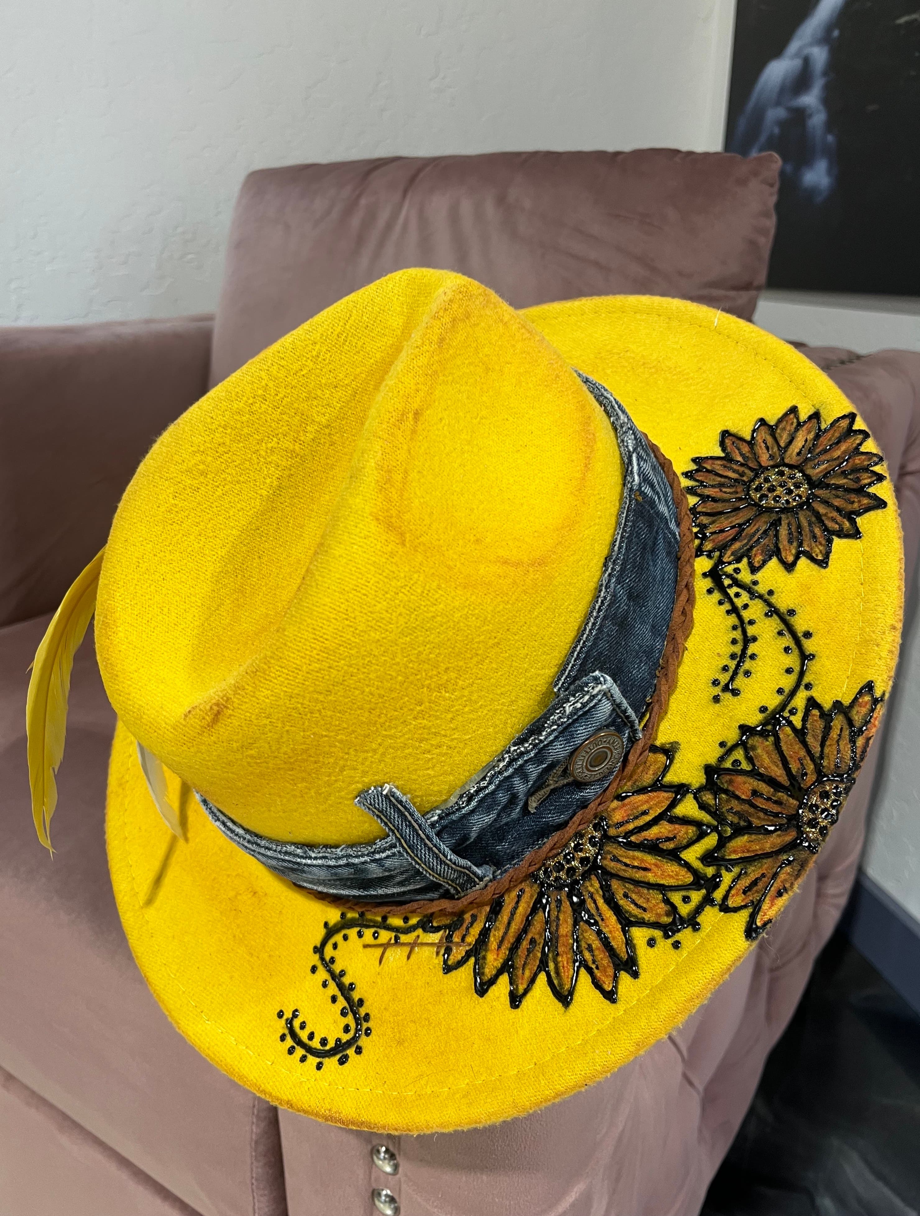 A vibrant yellow hat with sunflower embellishments and a denim band rests on a soft surface.