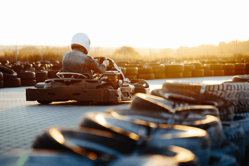 A go-kart racer speeds around a track lined with tires during sunset.