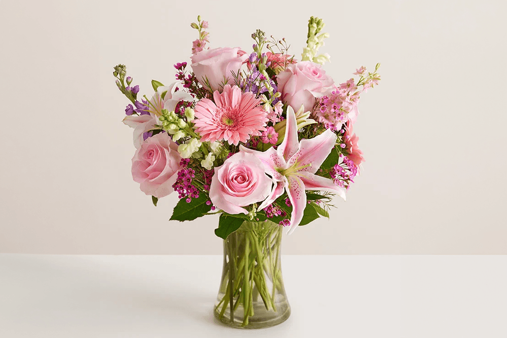 A vibrant bouquet of pink roses, lilies, and assorted wildflowers in a glass vase.