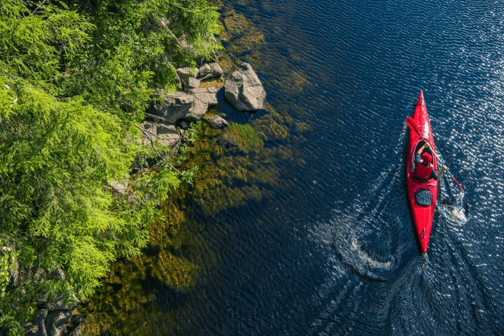 A kayaker paddles on a serene blue lake surrounded by lush greenery.