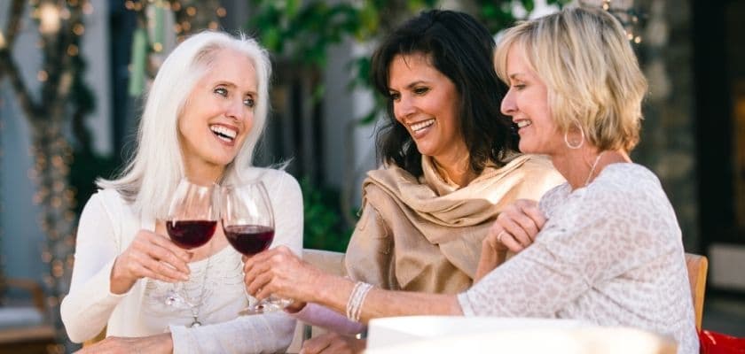 Three women joyfully clink glasses of red wine outdoors.
