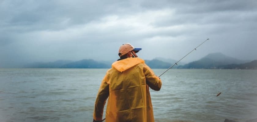 A person in a yellow raincoat fishing by a lake on a cloudy day.