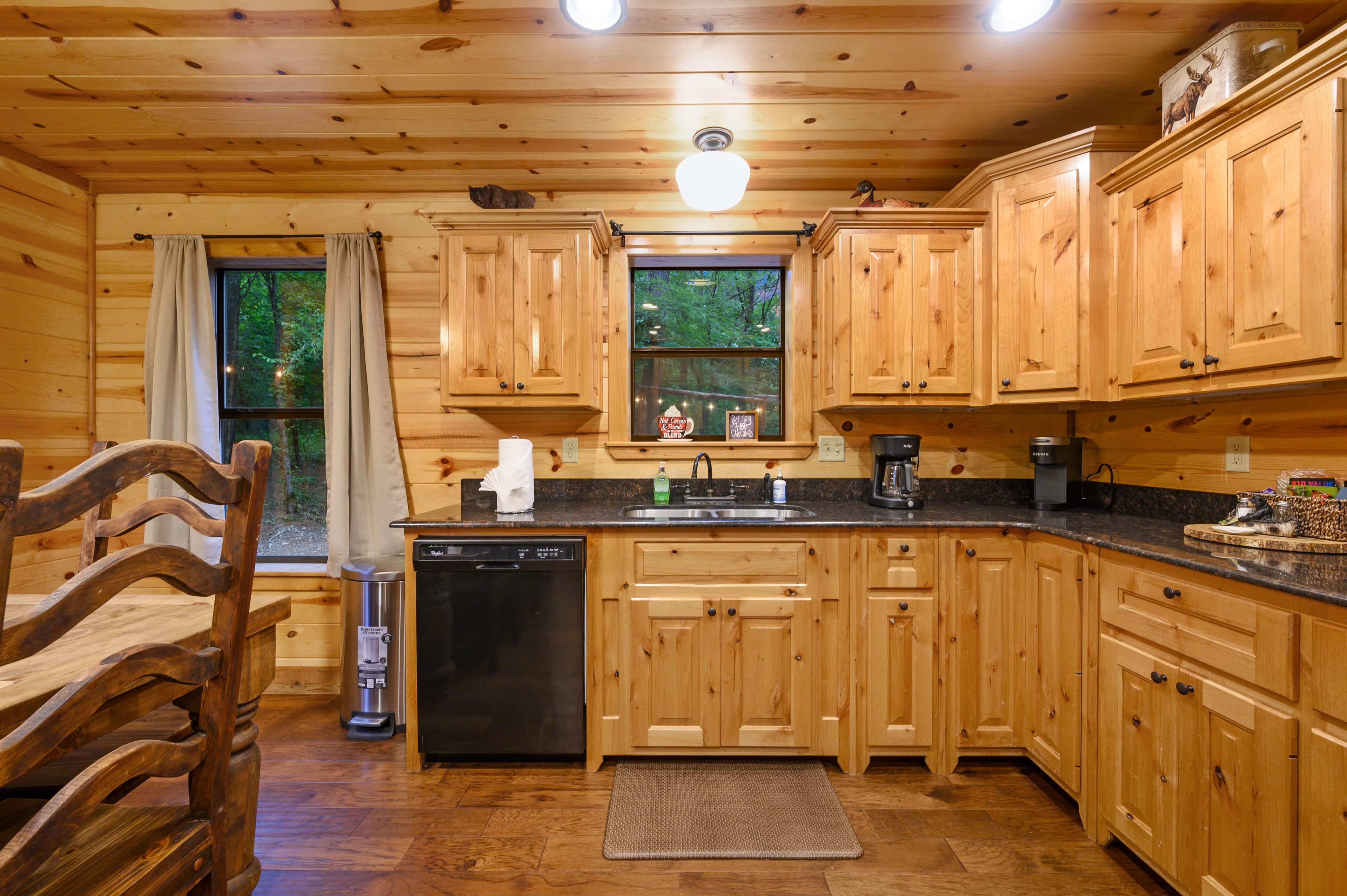 A cozy wooden kitchen featuring natural wood cabinets, a dark countertop, and a small dining area.
