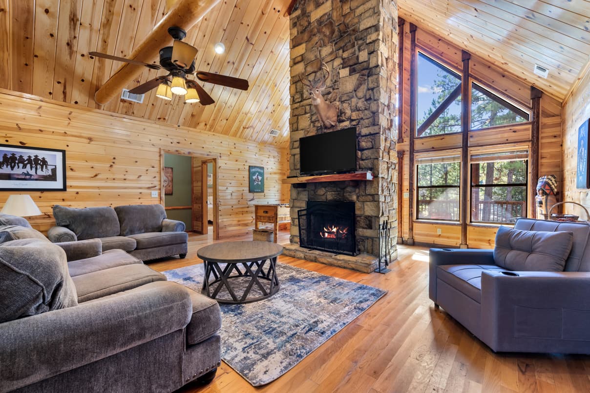 Cozy wooden living room with a stone fireplace, large windows, and comfortable seating.