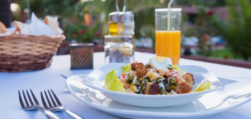 A fresh salad with croutons and a side of orange juice on a dining table.
