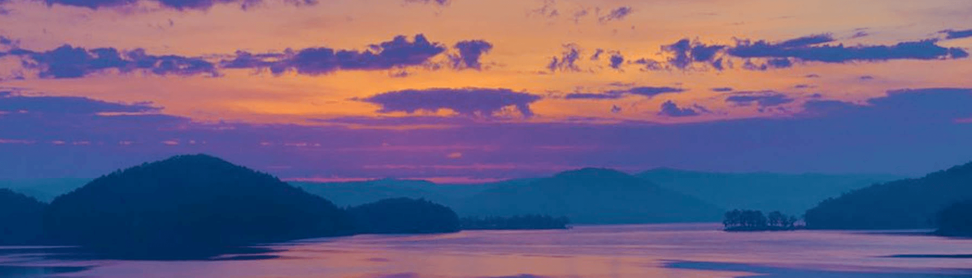 A serene sunset over a calm lake surrounded by rolling hills.
