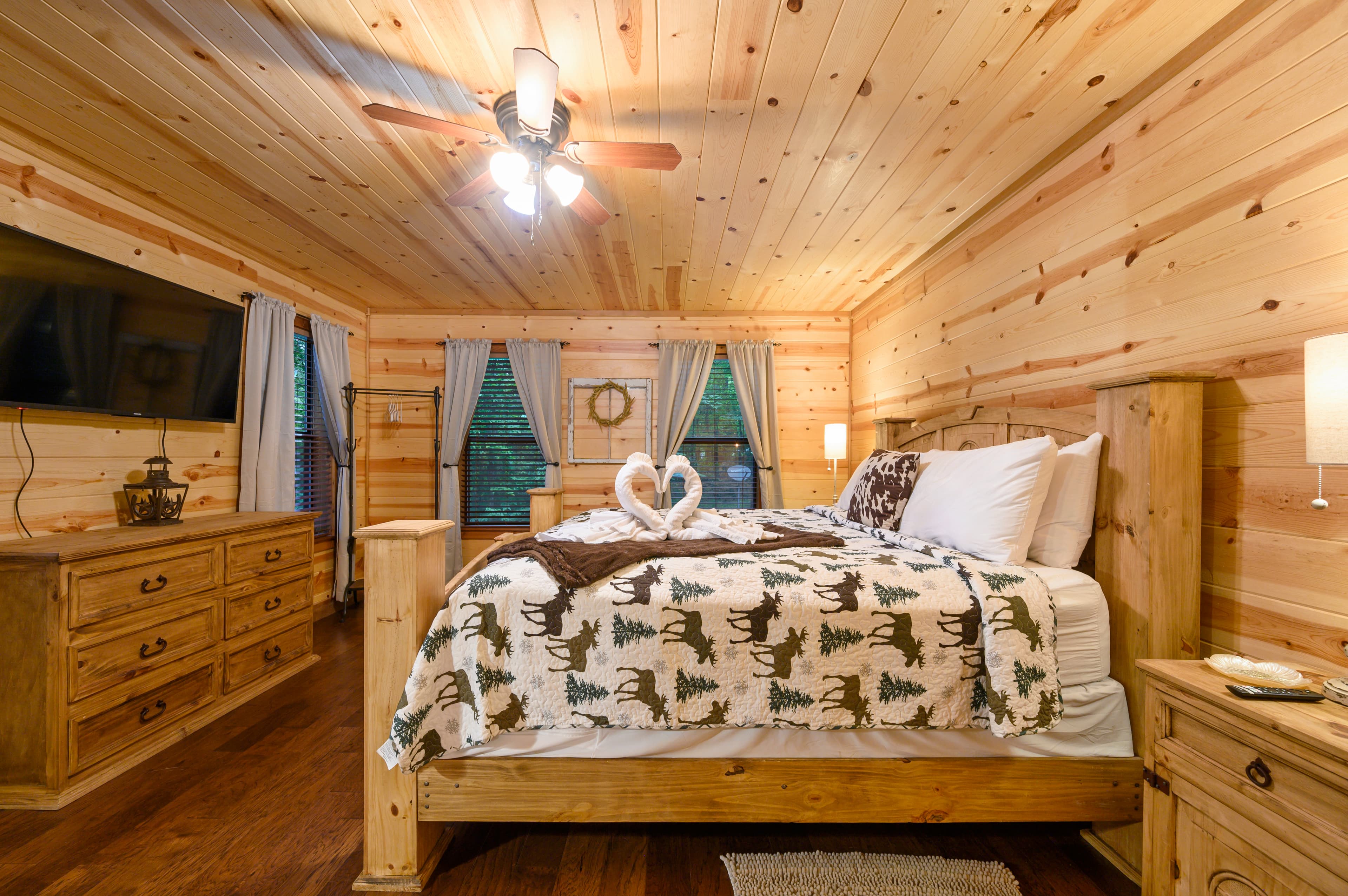 Cozy wooden bedroom featuring a bed with a patterned blanket and decorative swan towels, complemented by natural light and rustic decor.