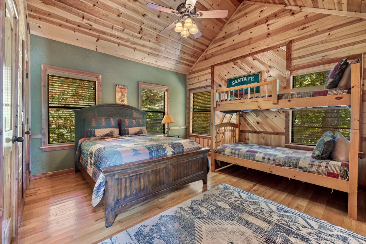 Cozy wooden bedroom featuring a queen bed, a bunk bed, and large windows with natural light.