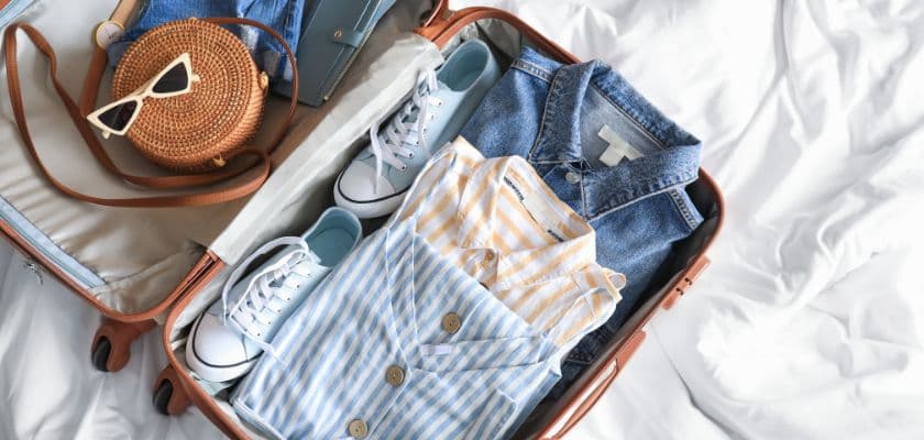 A neatly packed suitcase with clothes, shoes, and a round bag.