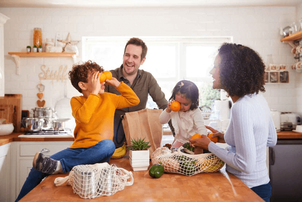 A joyful family enjoys time together in the kitchen while handling fresh fruits and groceries.