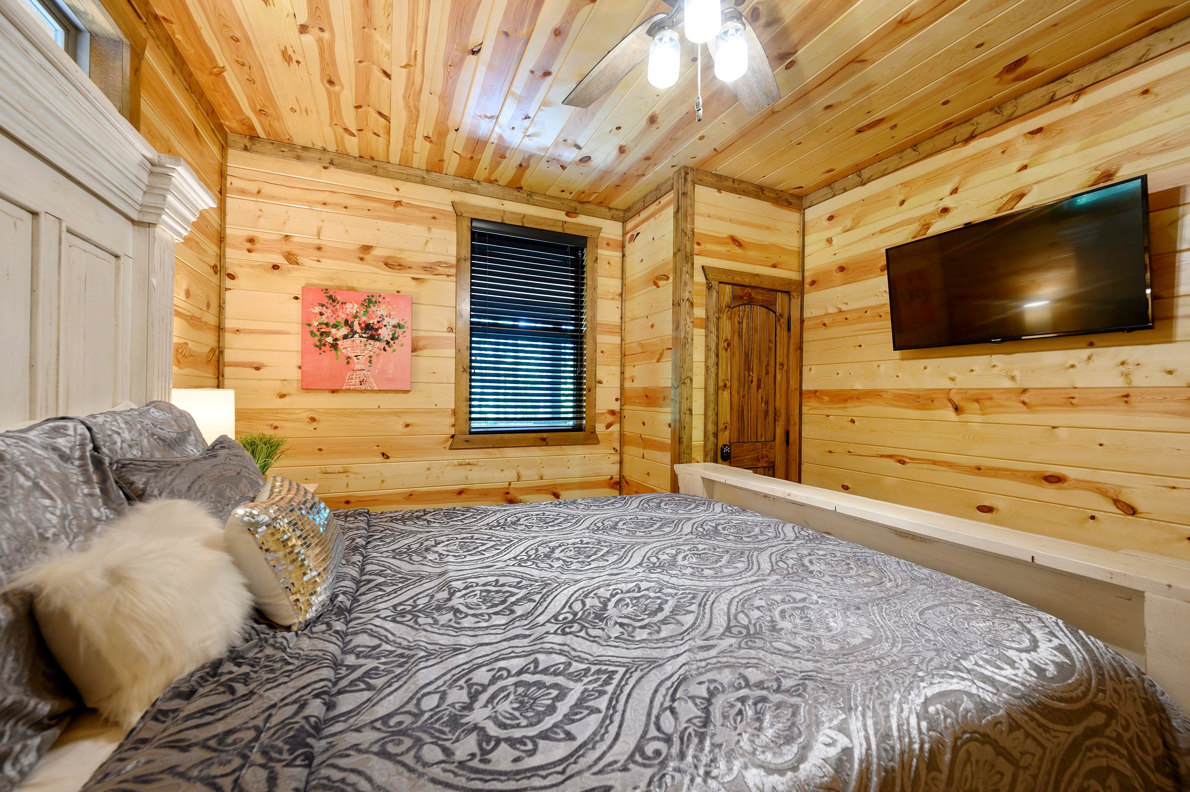 A cozy bedroom featuring a wooden interior, a large bed with decorative pillows, and a wall-mounted TV.