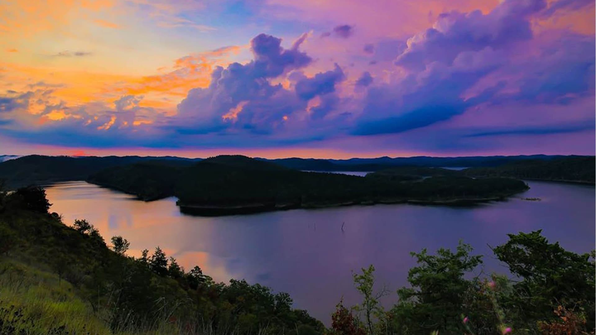 A serene landscape featuring a winding lake surrounded by hills and a colorful sunset sky.
