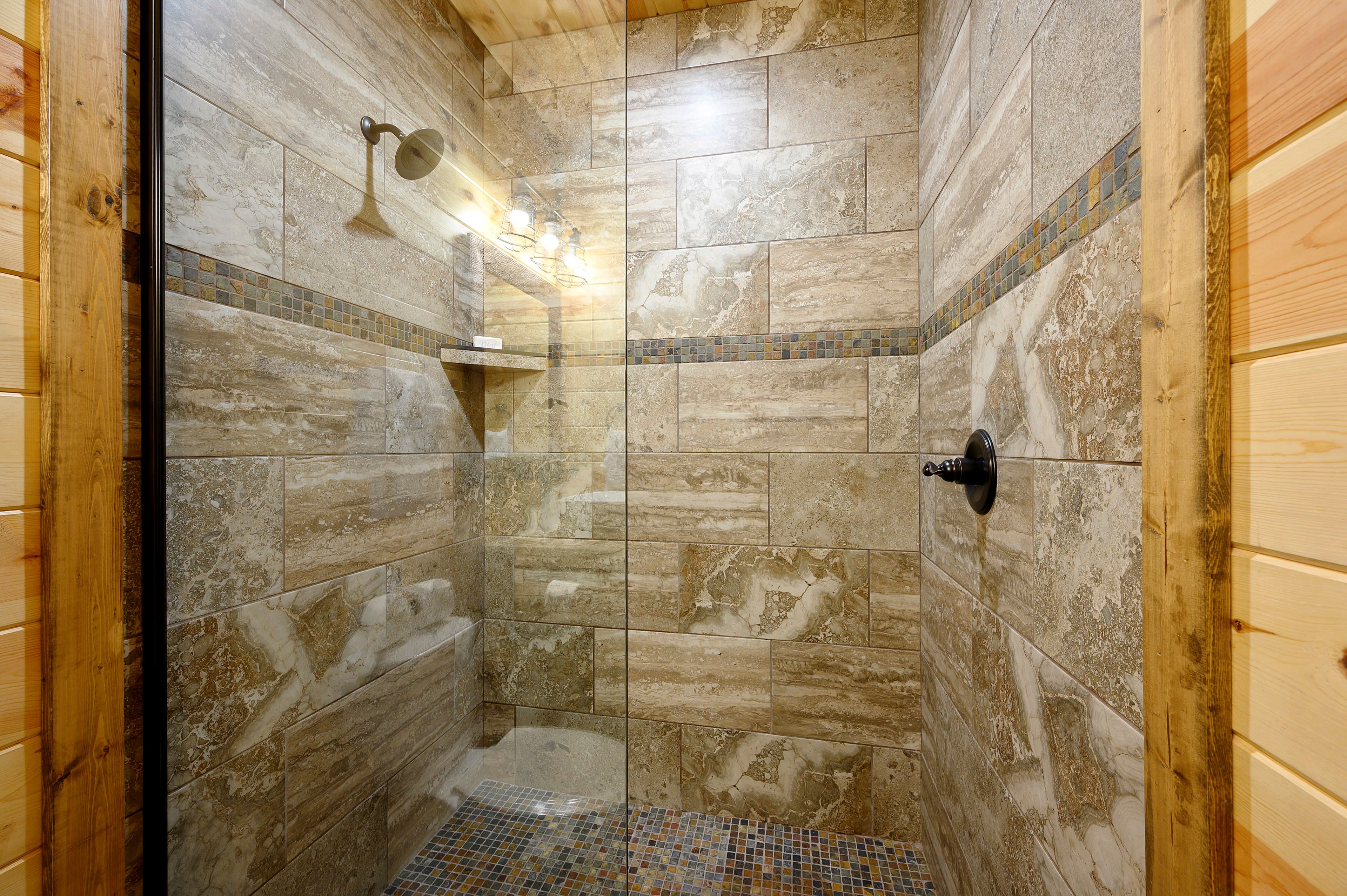 A modern shower with glass walls and stone tiles.