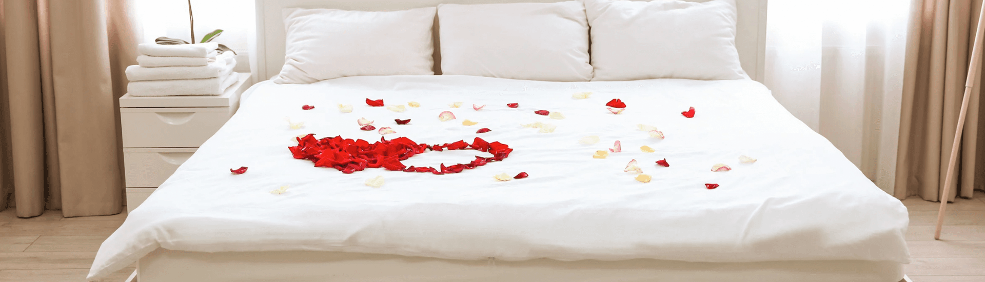 A bed adorned with rose petals and neatly stacked towels.