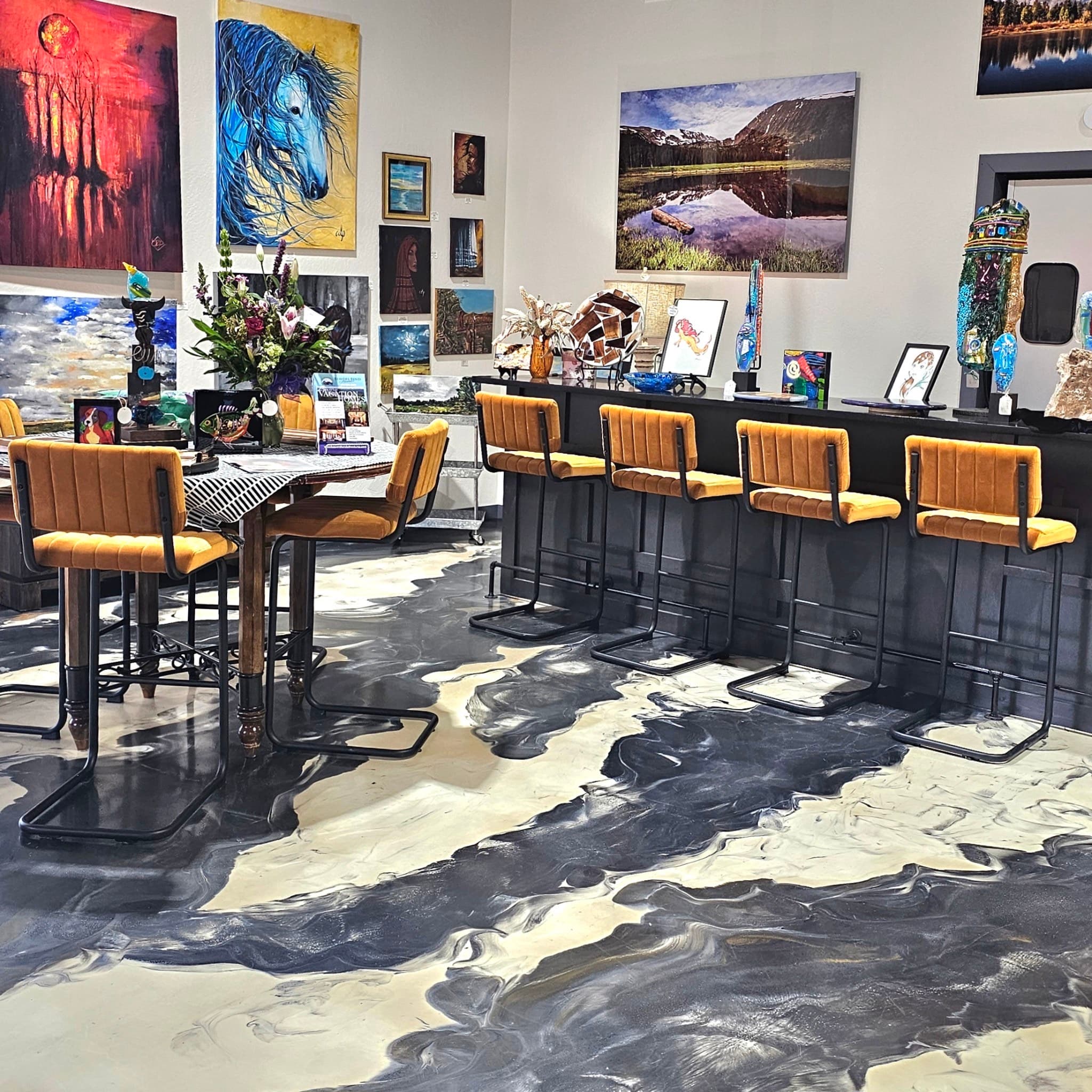 An art-filled café interior featuring a bar with orange stools and a unique marbled floor design.