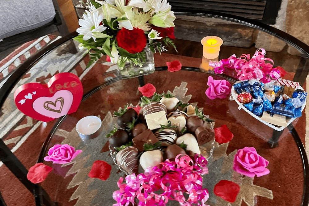 A beautifully arranged table featuring a bouquet of flowers, chocolates, a candle, and decorative hearts.