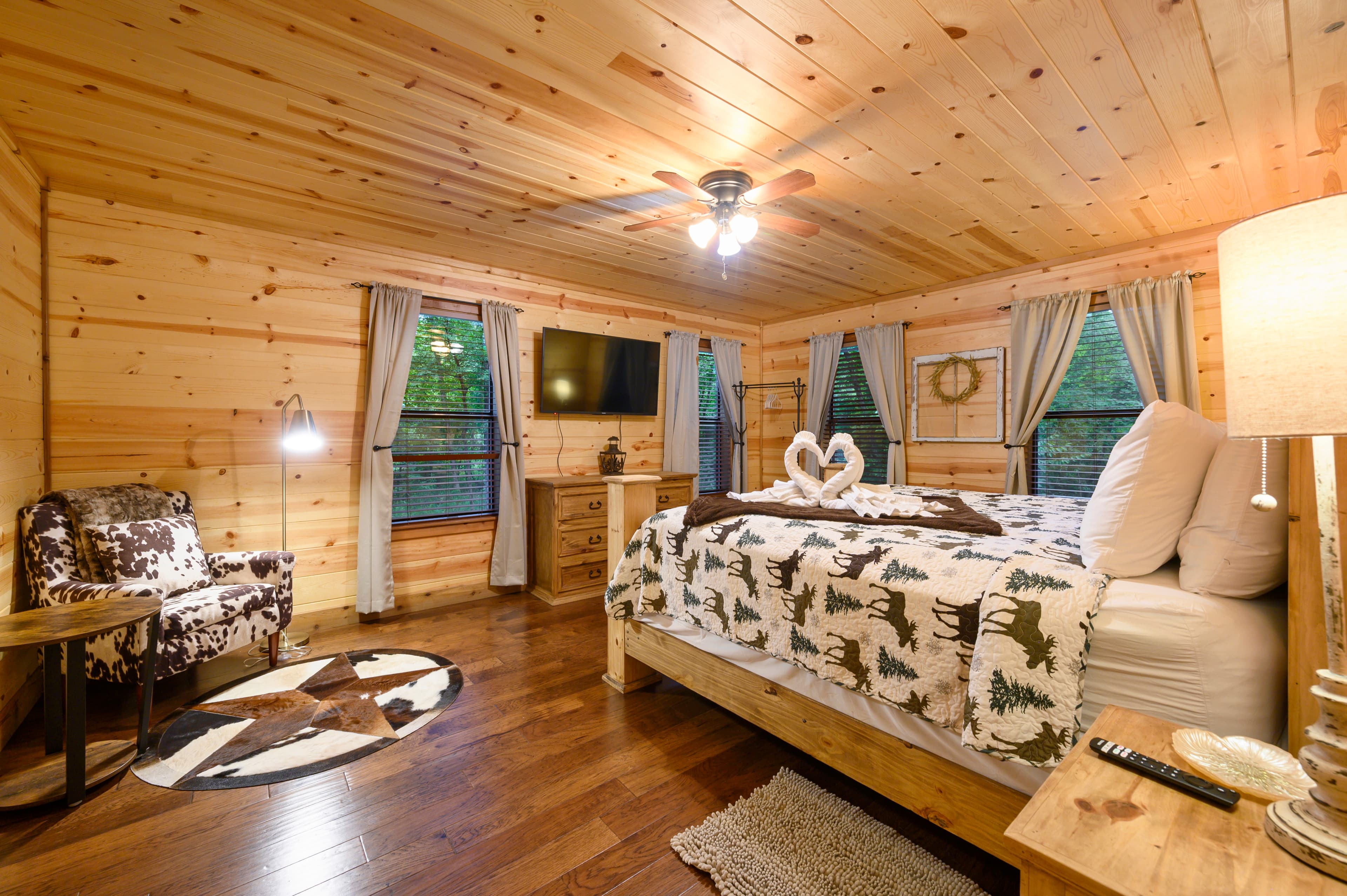 A cozy wooden bedroom featuring a king-sized bed, a patterned blanket, a TV, and rustic decor.