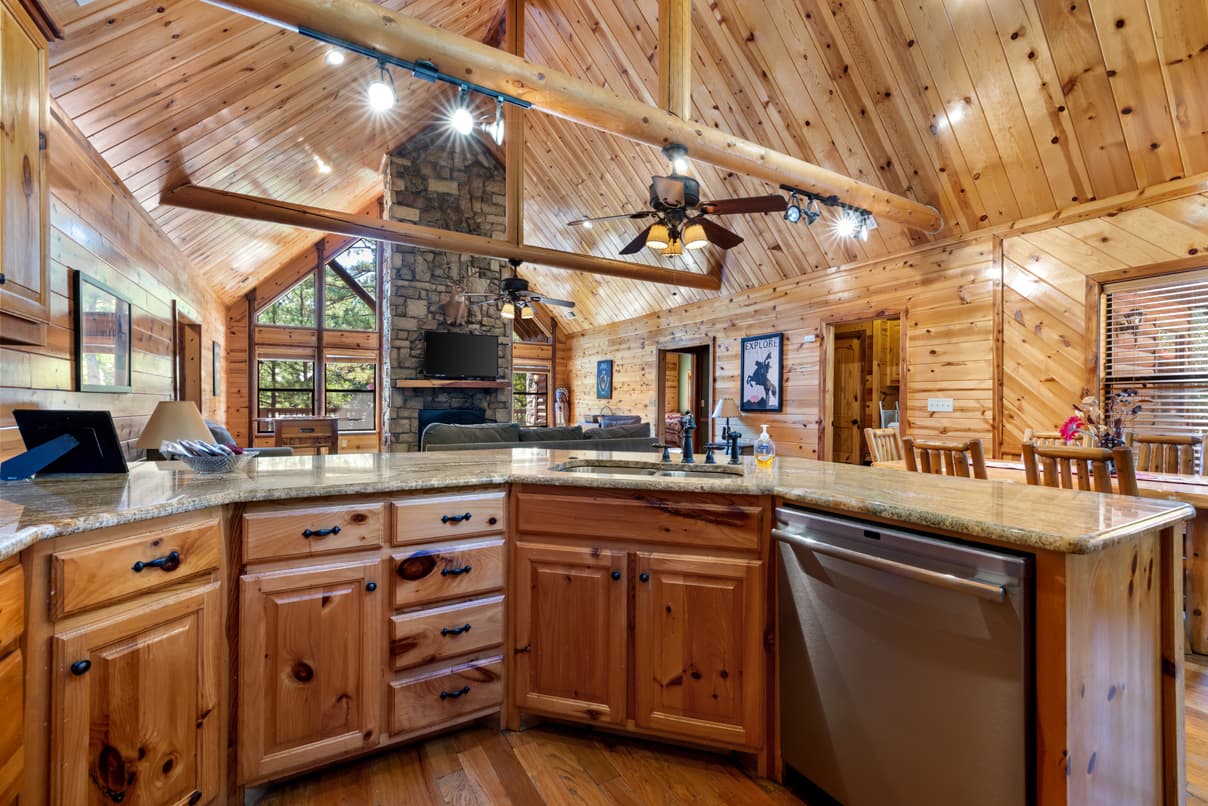A spacious wooden kitchen featuring a granite countertop and an open layout with a living area in the background.