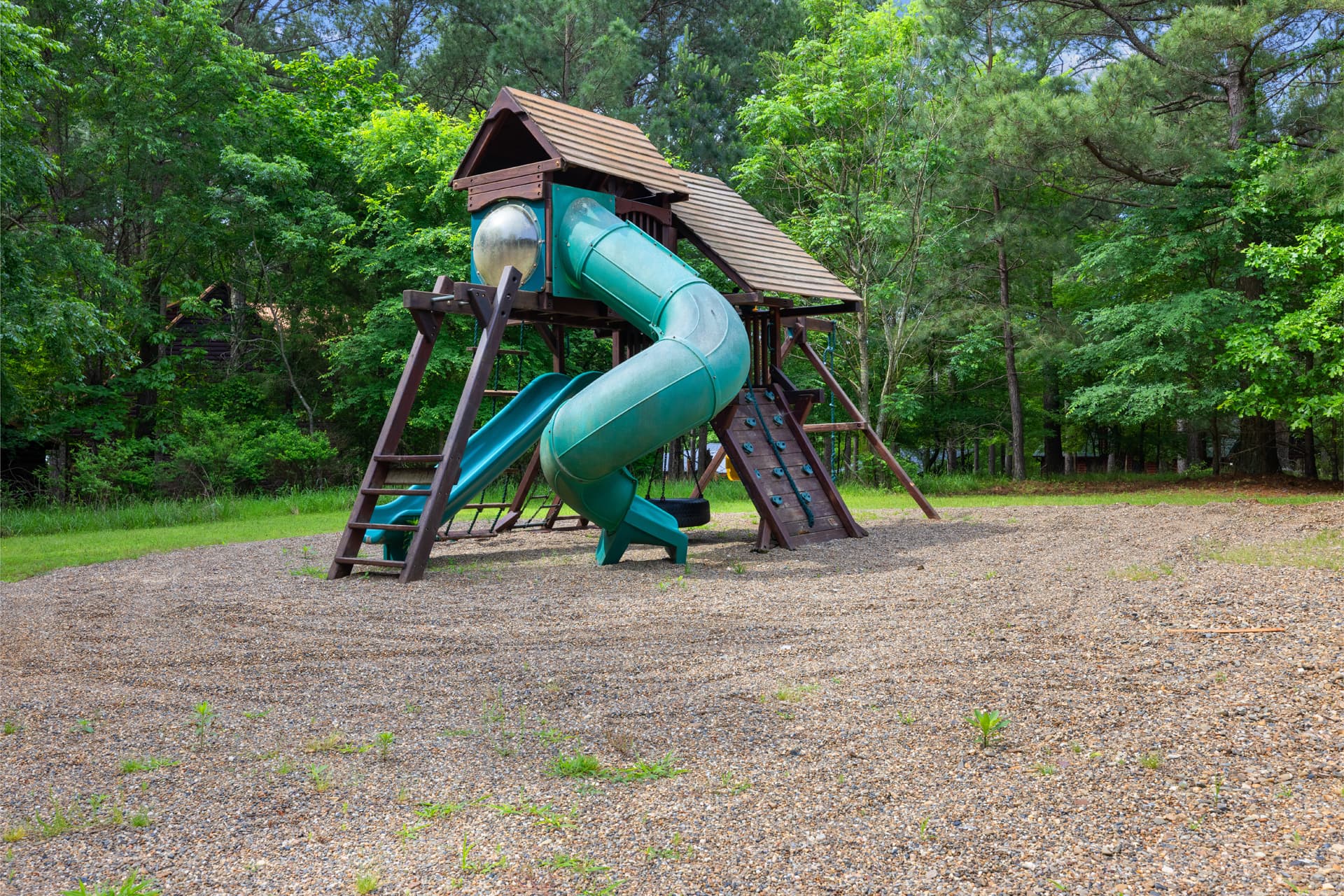 A green slide on a wooden playground structure surrounded by greenery.