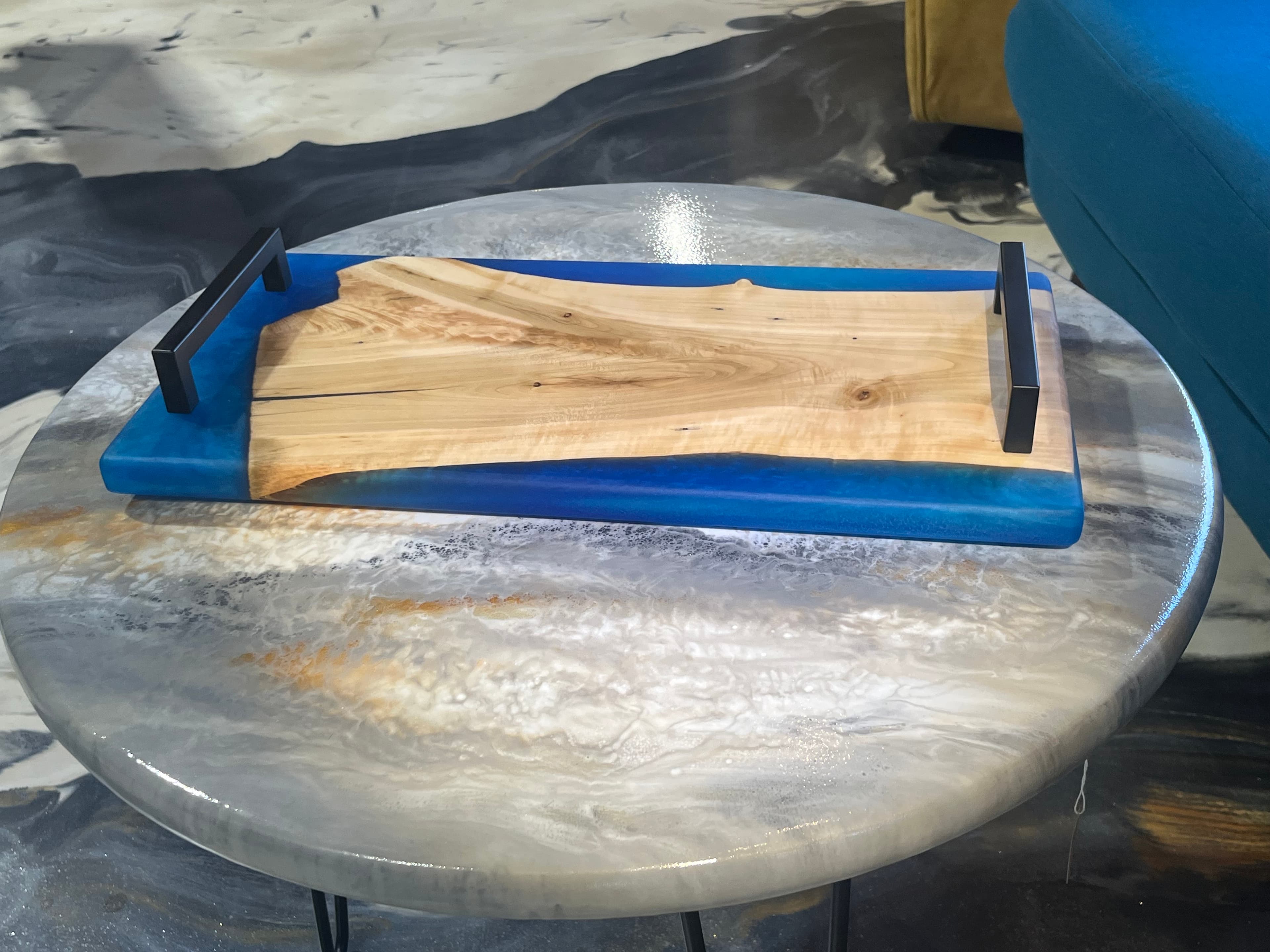 A wooden serving tray with blue resin edges rests on a marbled table.