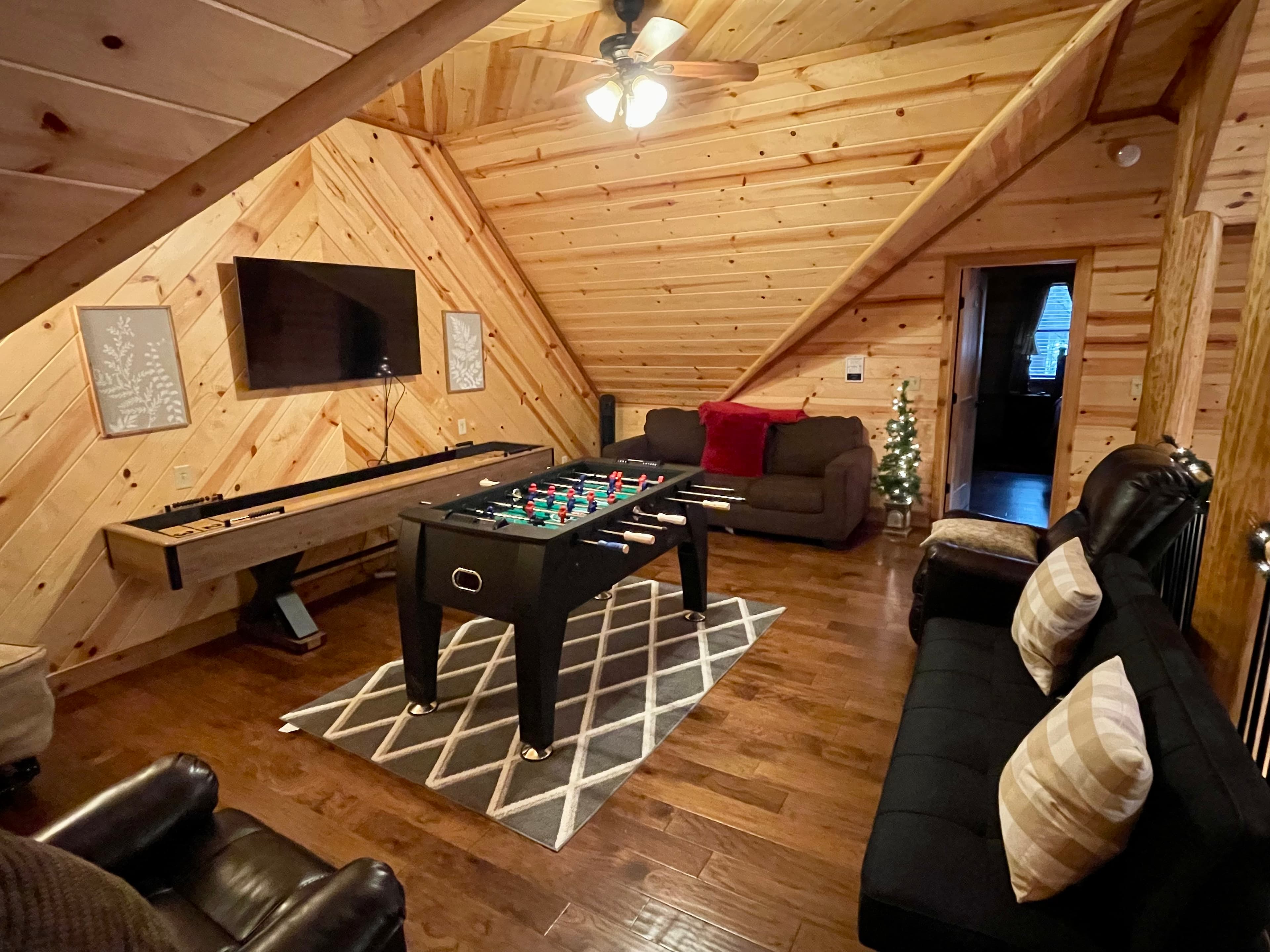 Cozy wooden room featuring a foosball table, a TV, and comfortable seating.
